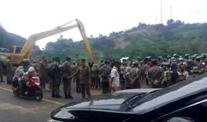 sekelompok petugas keamanan dan personel militer yang berkumpul di dekat sebuah alat berat di tepi jalan pada Senin 11 November 2024
